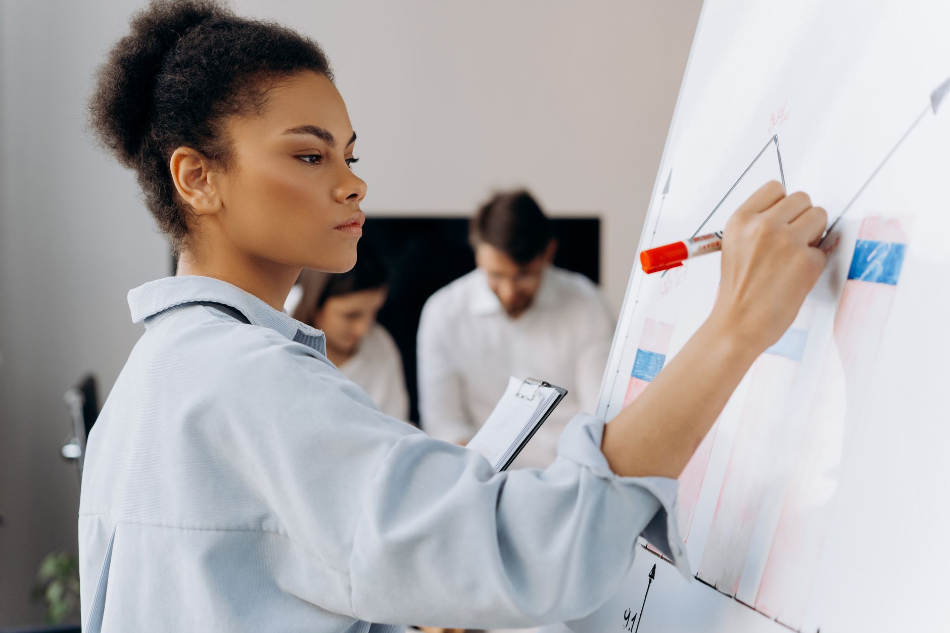 Sustainable Risk Management — Confident businesswoman illustrates data on whiteboard during a team meeting, showcasing collaborative analysis.