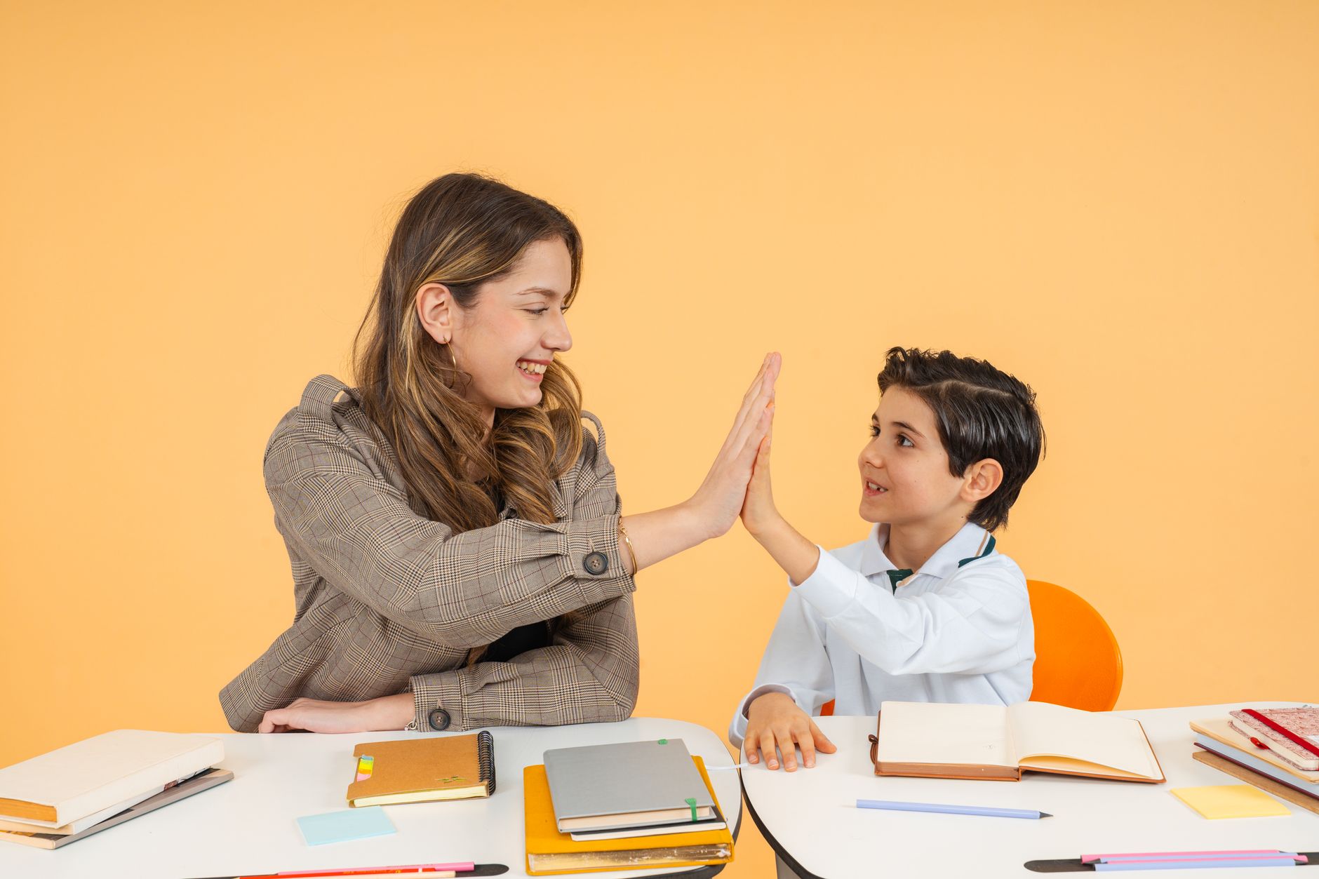 The Development of Psychological Attachments — Teacher and student sharing a high-five over a desk in a bright classroom, fostering a positive learning environment.