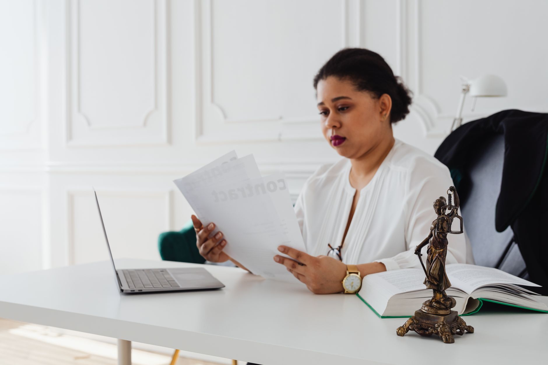 Contract Law — Black woman lawyer reading legal papers at her desk in a modern office.