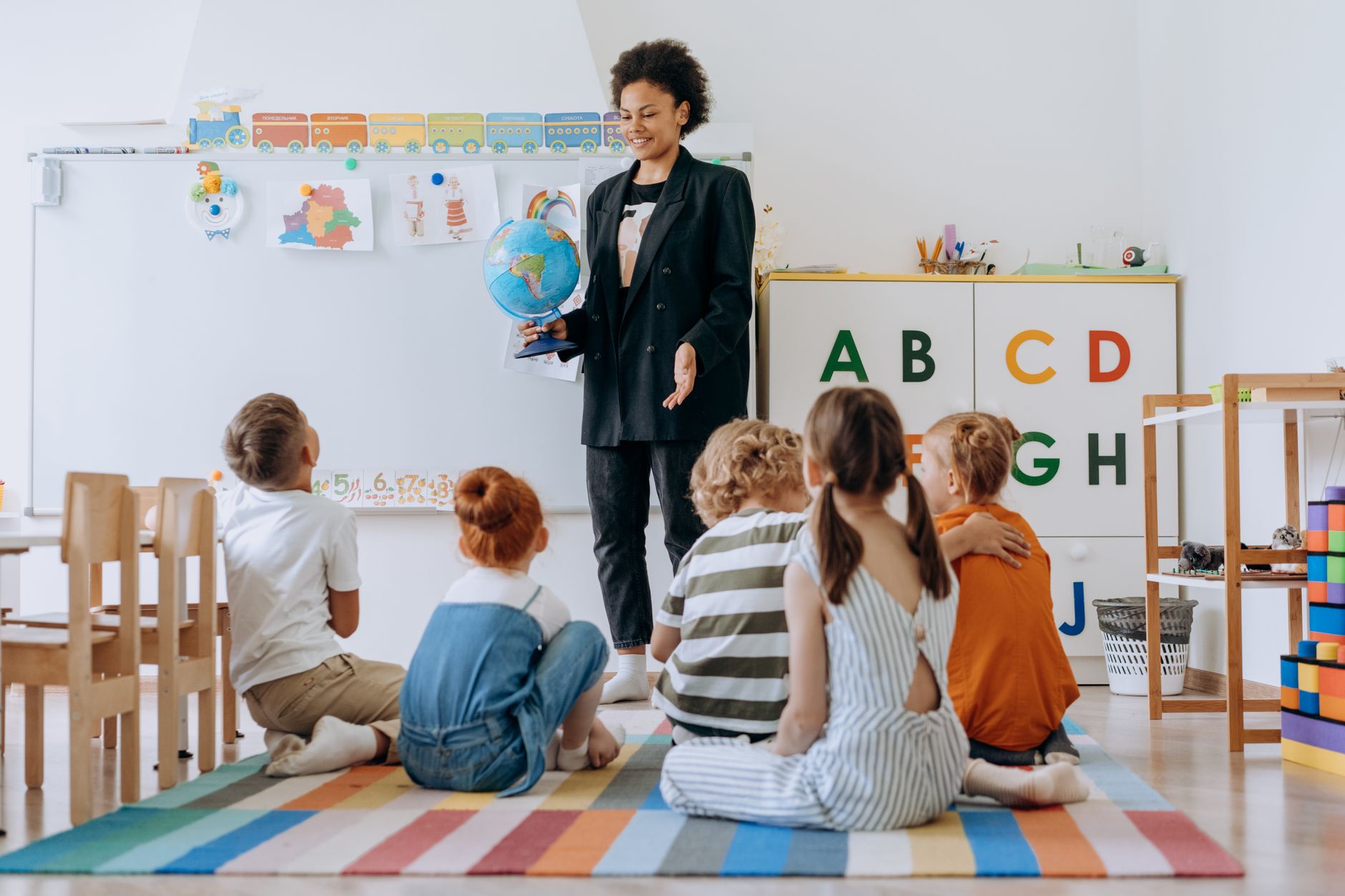 Teaching receptive skills: listening and reading — Teacher interacts with a group of young students in a vibrant classroom setting, using a globe for educational activities.