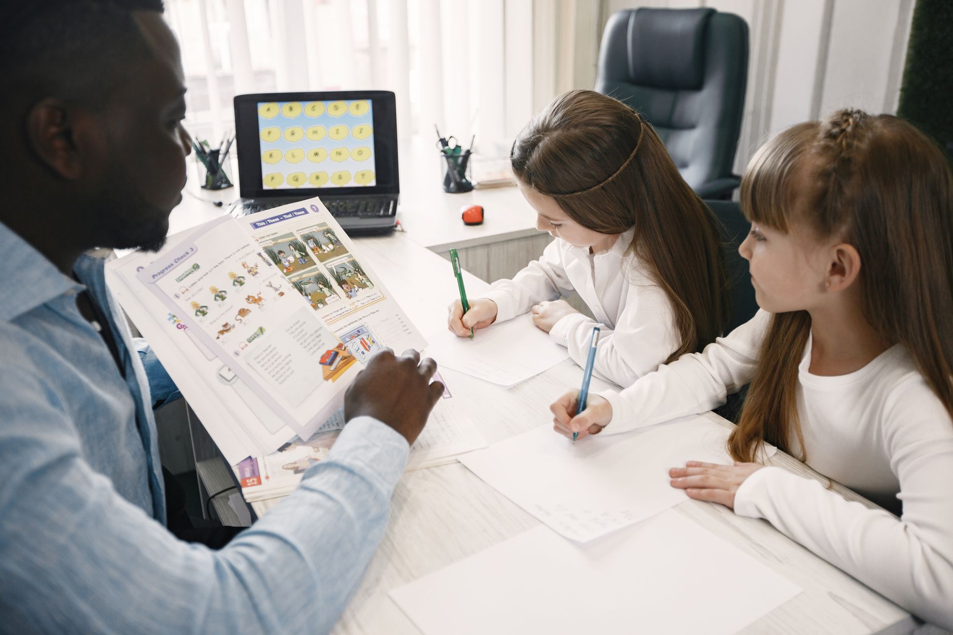 Teaching productive skills: speaking and writing — A teacher instructing two young students in a classroom environment.