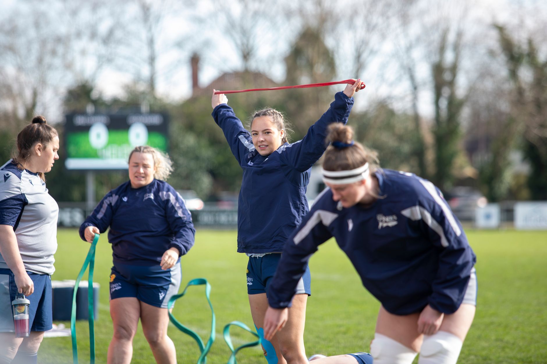 Health and Physical Success of Female Athletes — Female rugby team training outdoors with resistance bands on a sunny day.