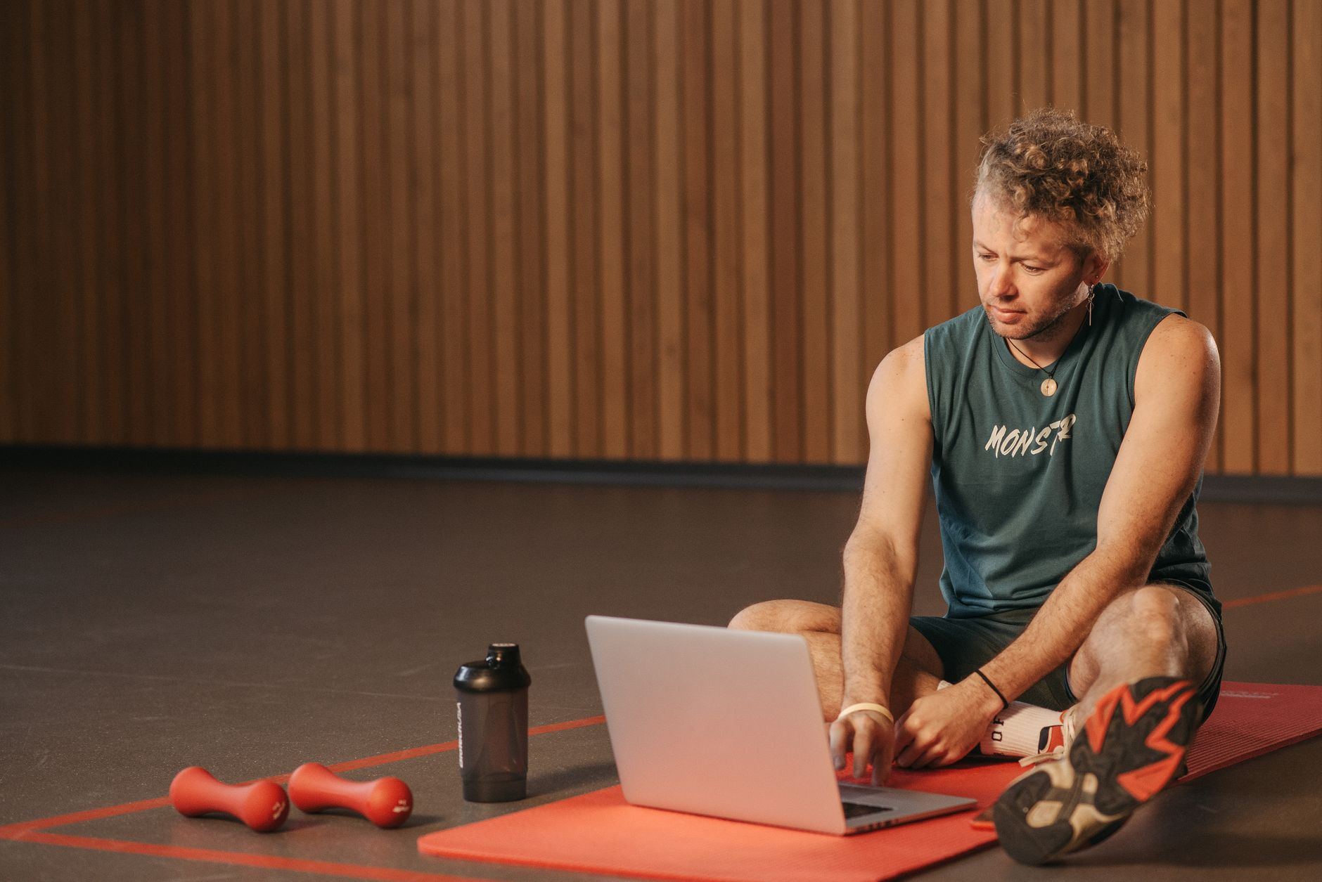 Strength and Conditioning for Cricket — Man sitting on exercise mat with laptop, surrounded by dumbbells, creates a unique fitness workspace.