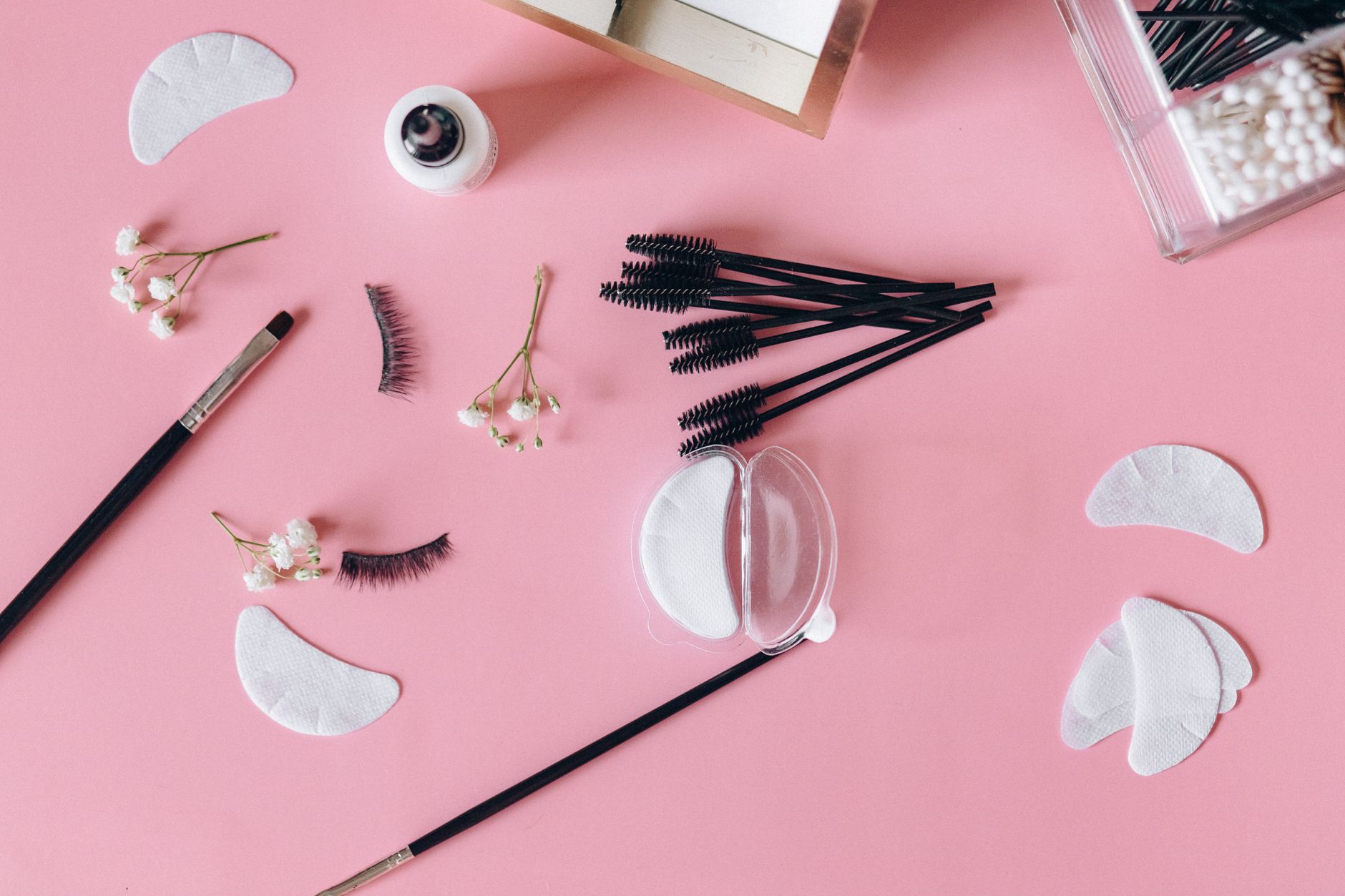 Advanced semi-permanent lash extensions — Aesthetic makeup tools and beauty items arranged on a pink surface.