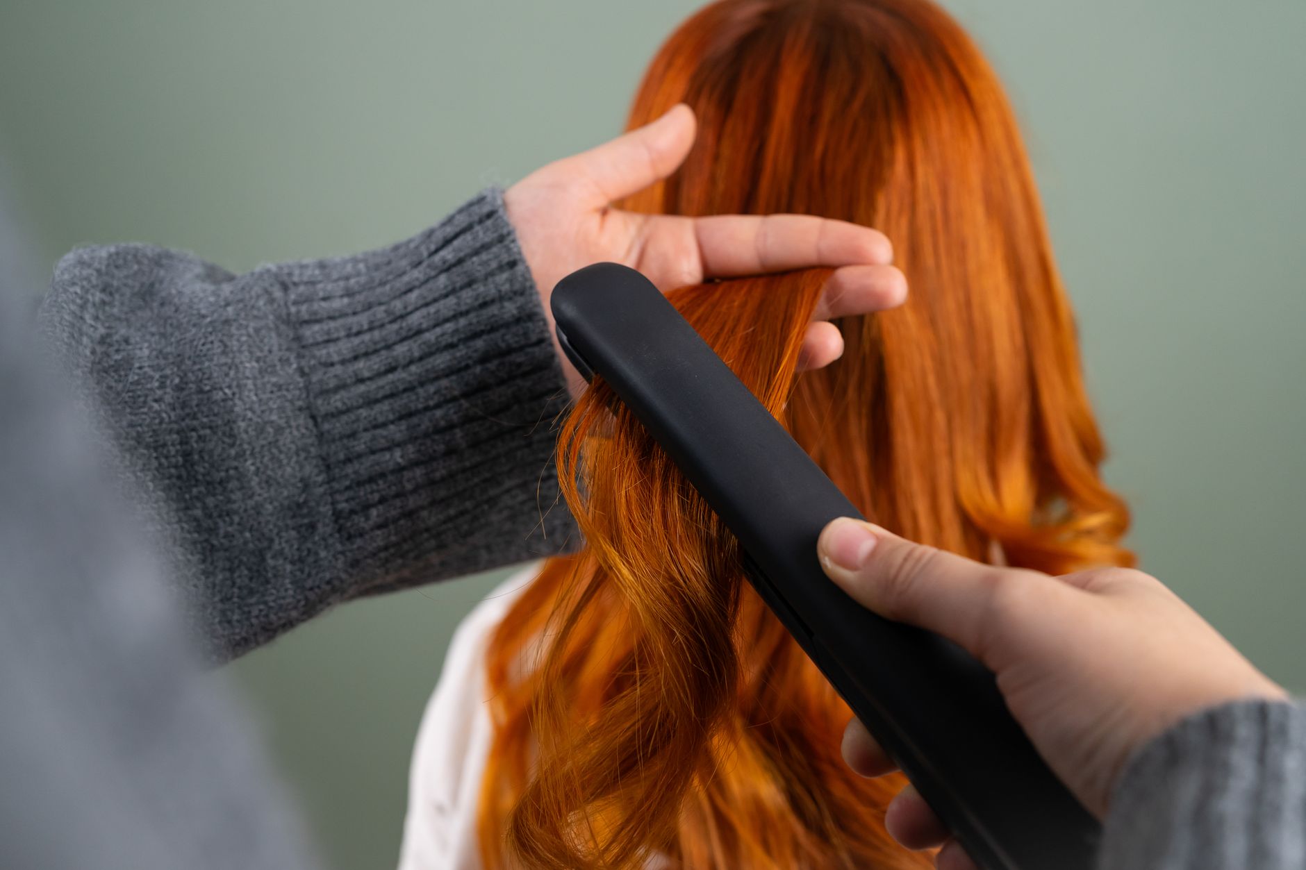 Colour and lighten hair — Hands styling long red hair using a flat iron indoors. haircare and beauty concept.