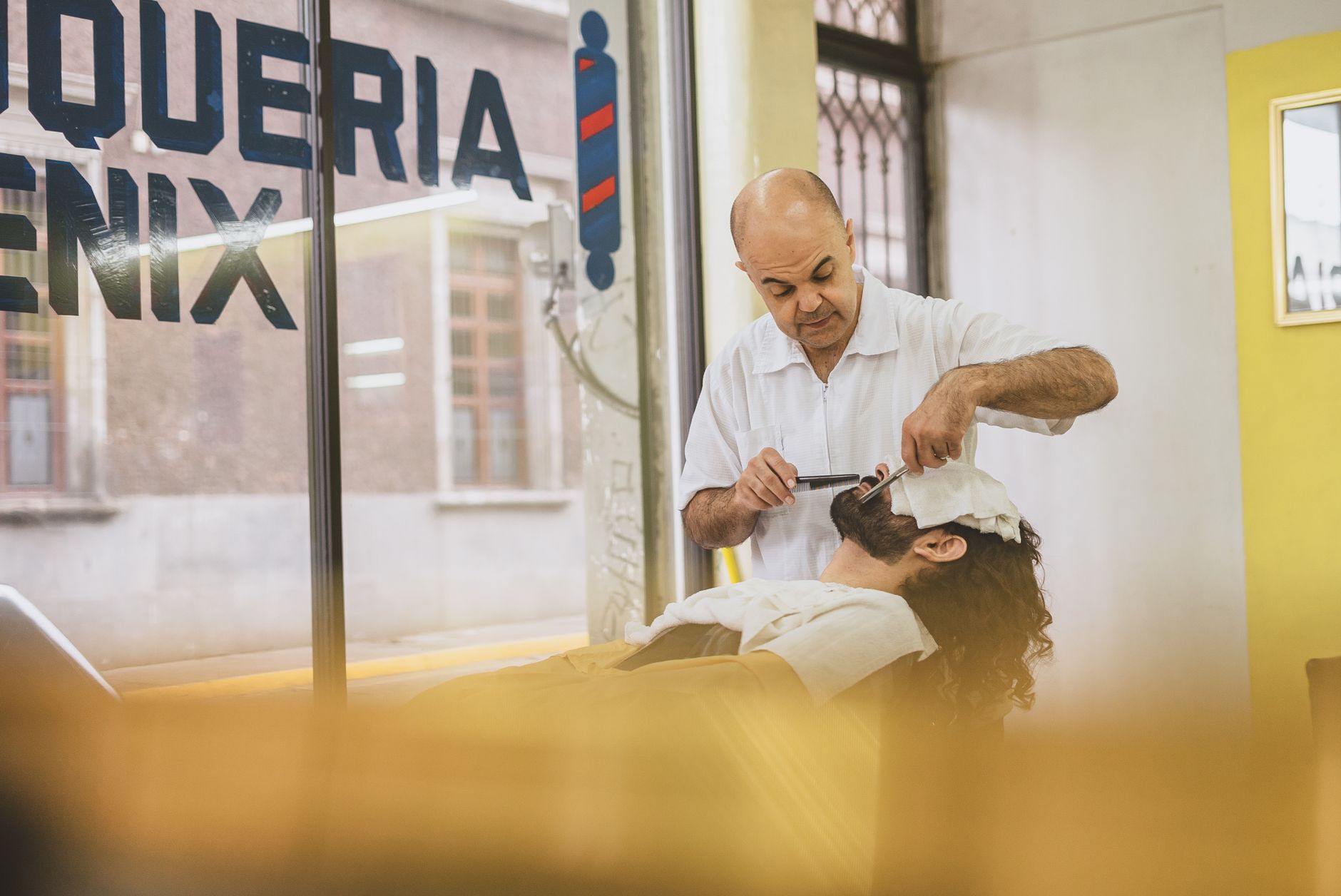 Relax hair — Barber performing a classic straight razor shave on a client in a bright barbershop.