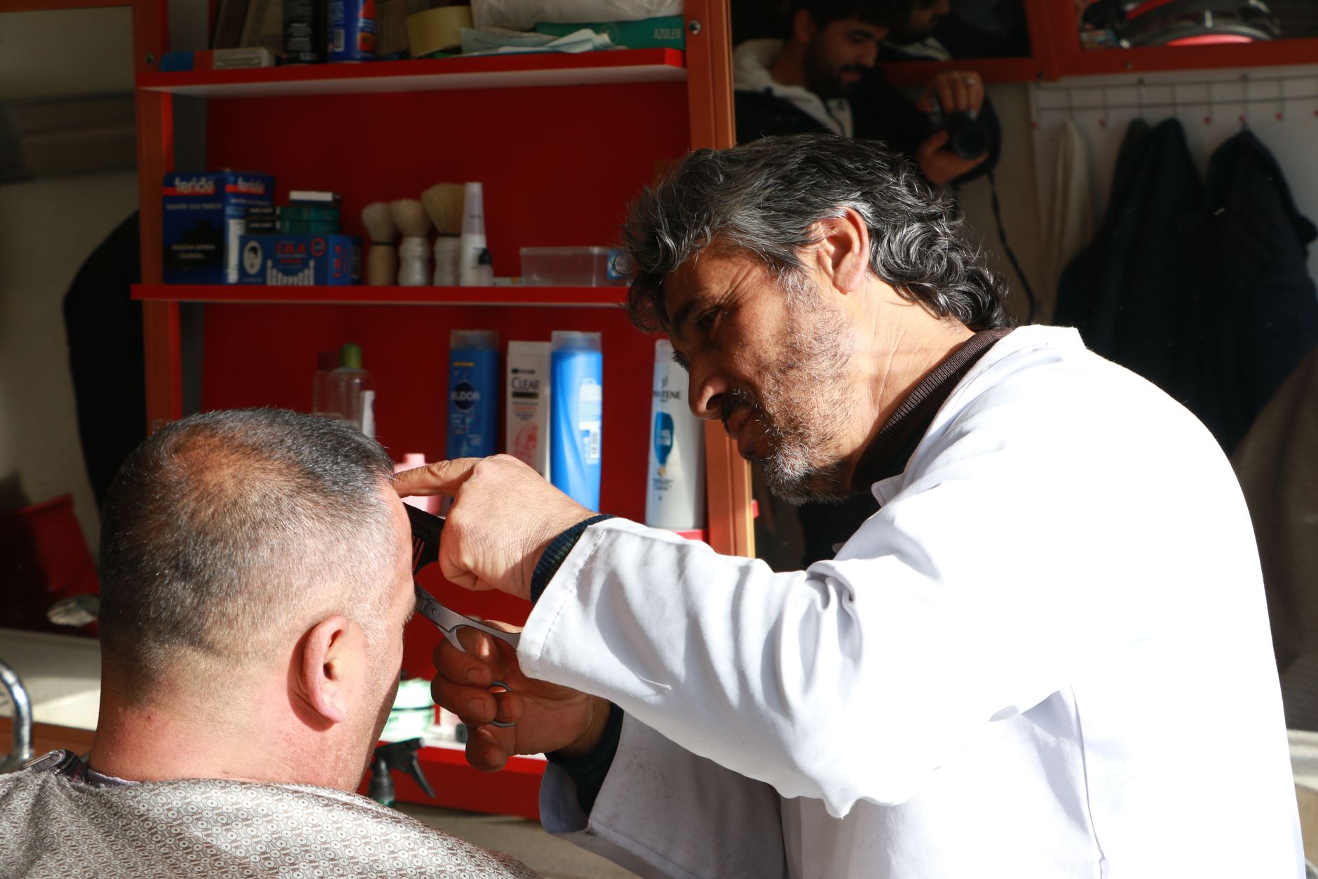 Freelance worker — A barber focuses on cutting a customer's hair in a well-equipped barbershop.