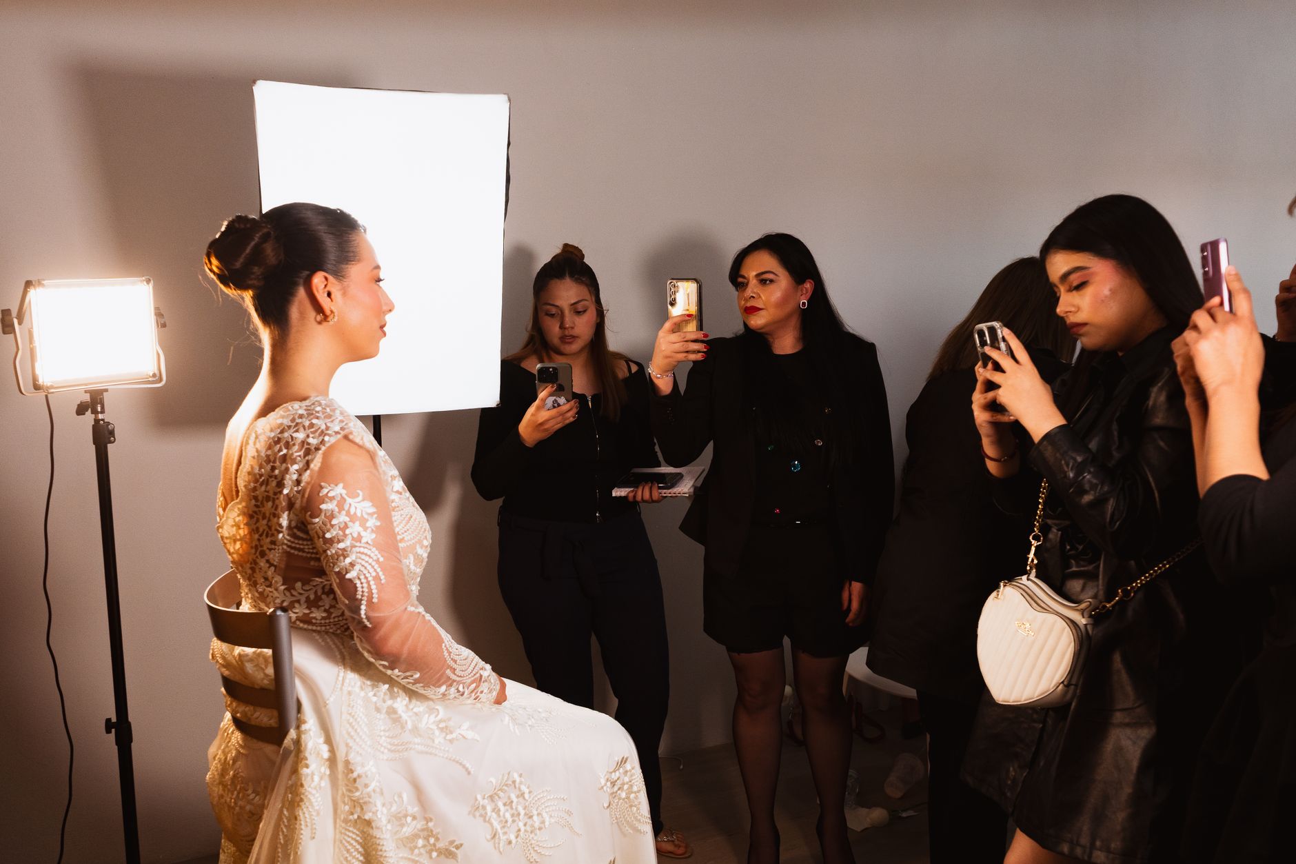 Creatively set, dress, style, and finish hair — Bride sitting indoors, getting artistic makeup applied by professionals in mexico city.