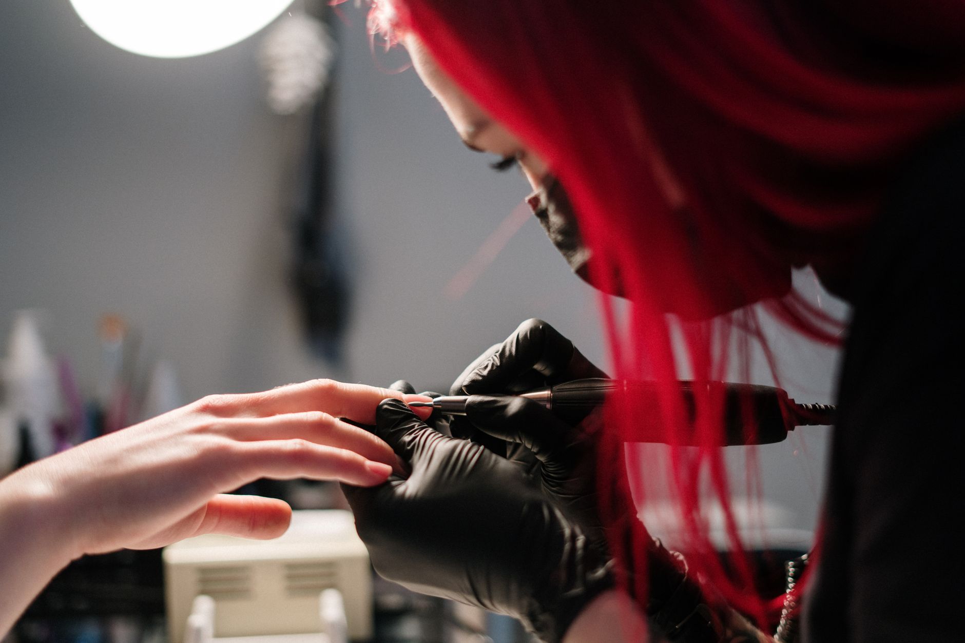 Colour correction — A nail technician with red hair performs a manicure wearing black gloves in a salon.
