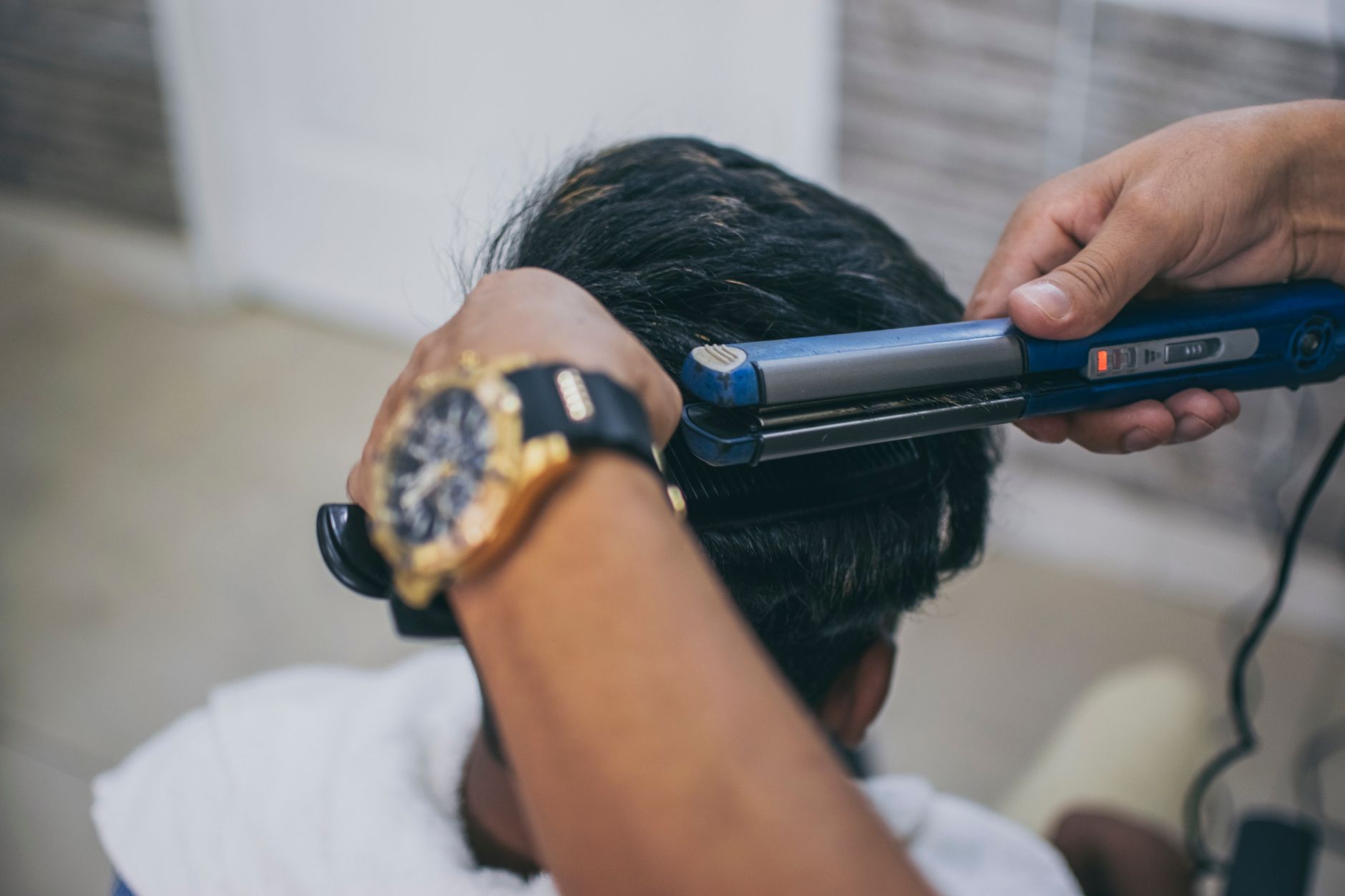 Smooth and strengthen hair — Close-up of a hairdresser styling a client's hair using a straightener in a barbershop.