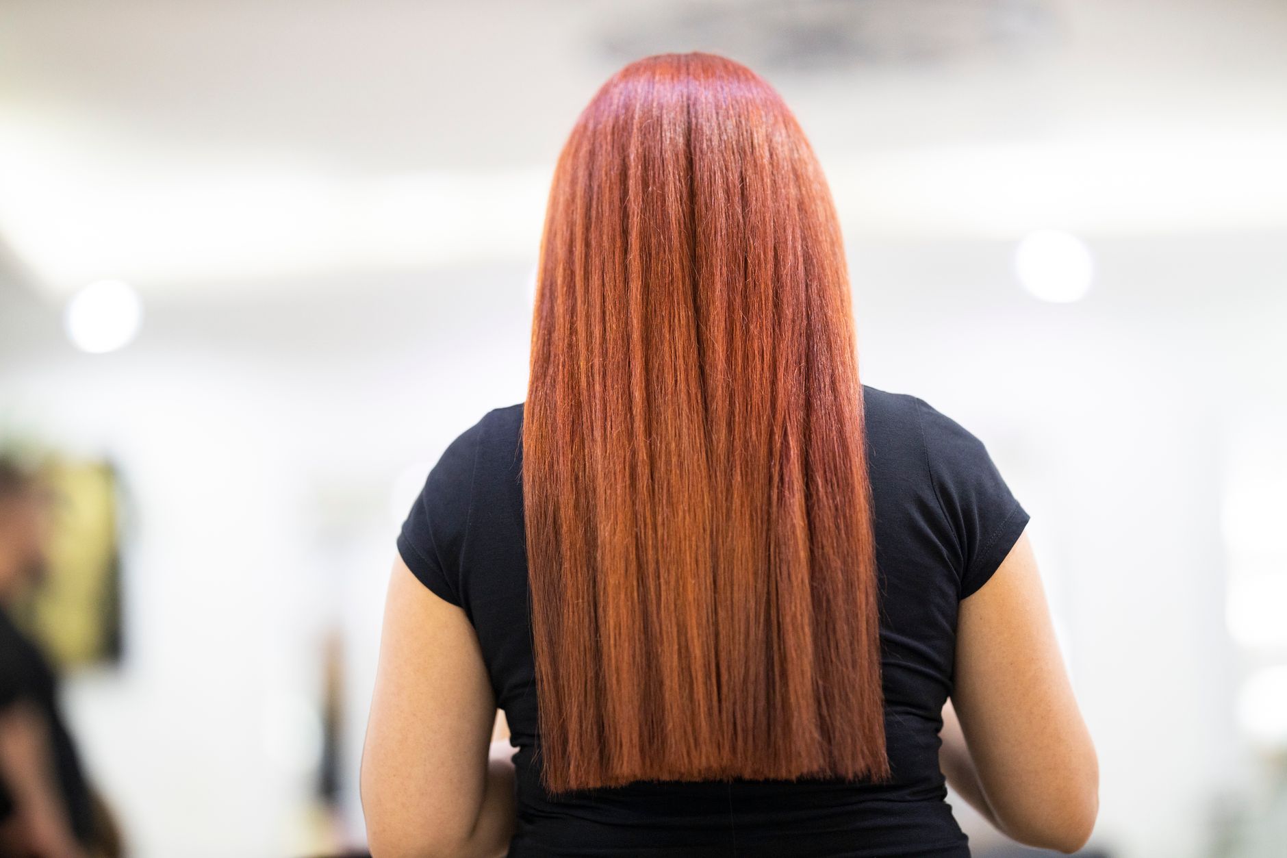 Cultivate, maintain, and repair locks — A woman with straight, vibrant red hair seen from the back, showcasing a fresh hairstyle in a professional salon.