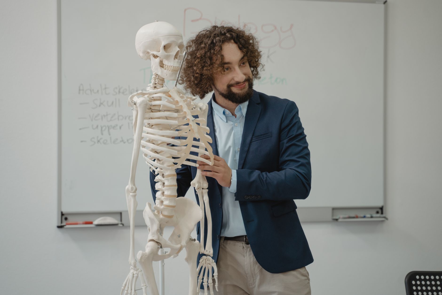Anatomy, physiology and pathology — A biology teacher demonstrates the human skeleton model in an engaging classroom setting.