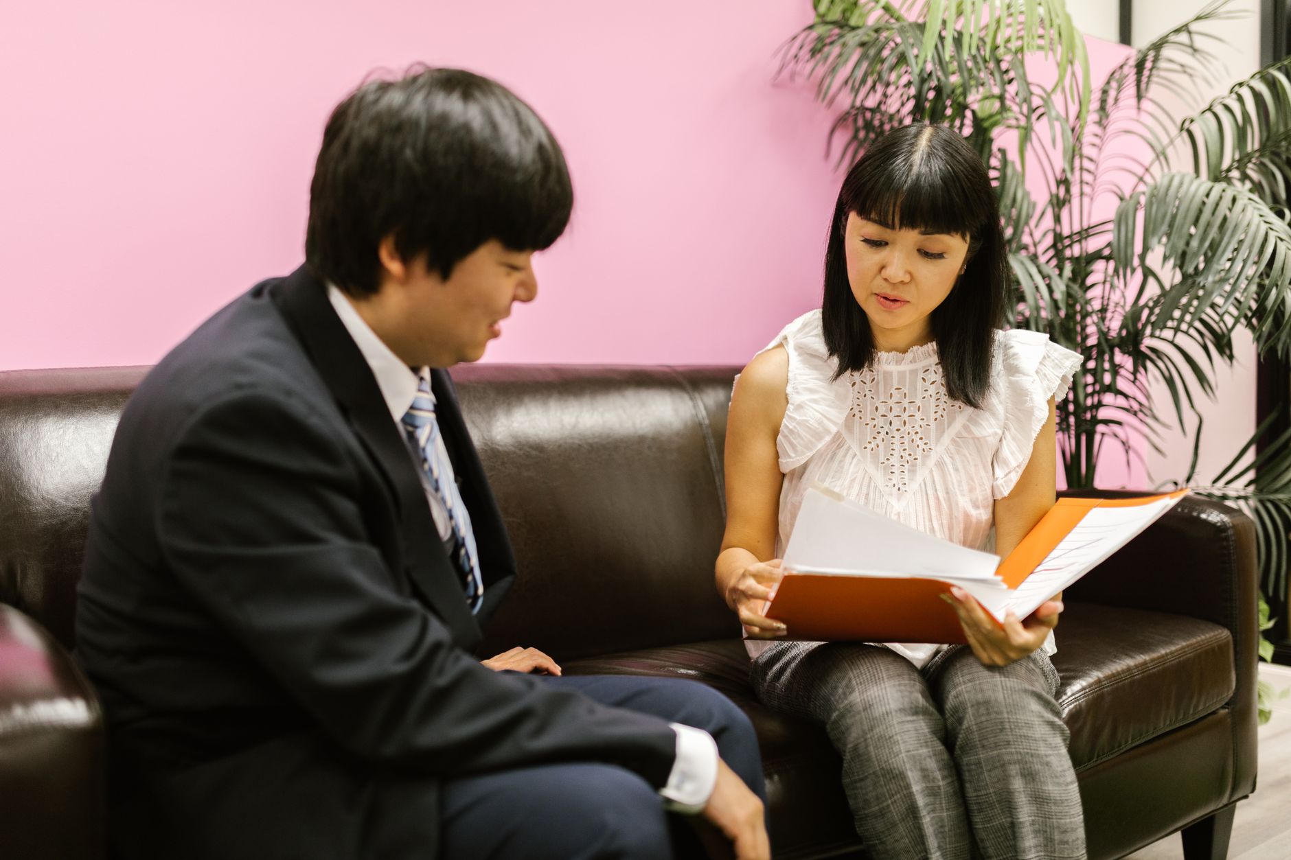 Client consultation and profiling — Two business professionals discussing documents on a sofa in an office setting.