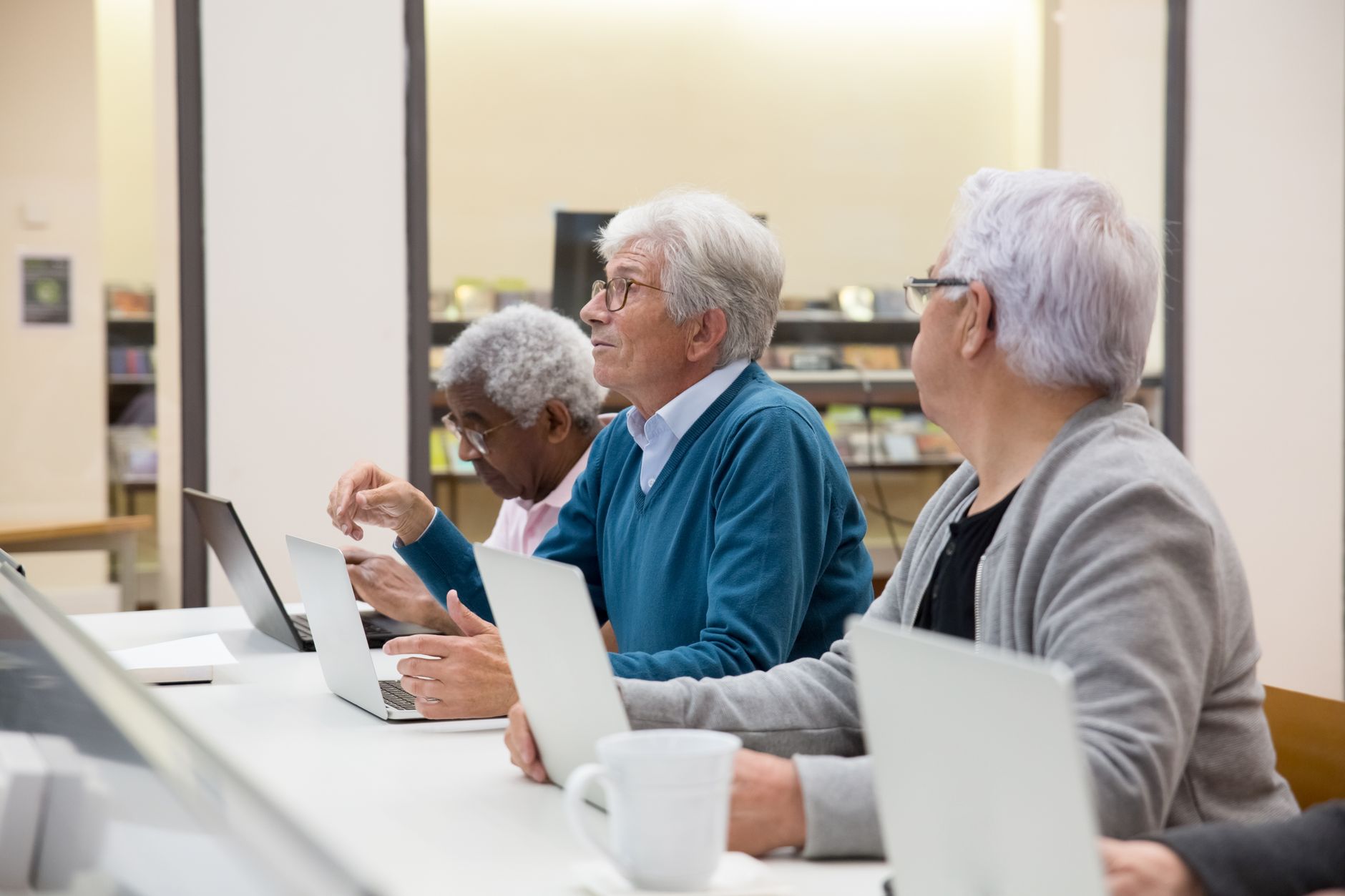 Promotional activities — Elderly men using laptops in a modern tech class, learning digital skills.