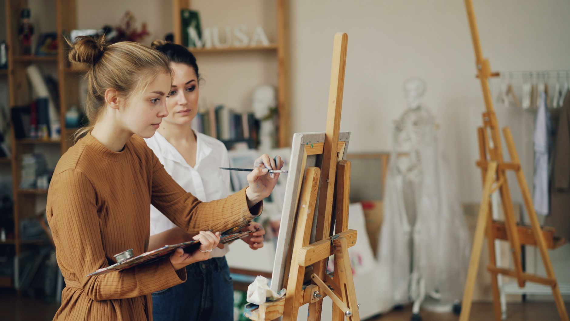 Implement health, safety, and hygiene — Two women focused on painting at easels in a creative art studio.
