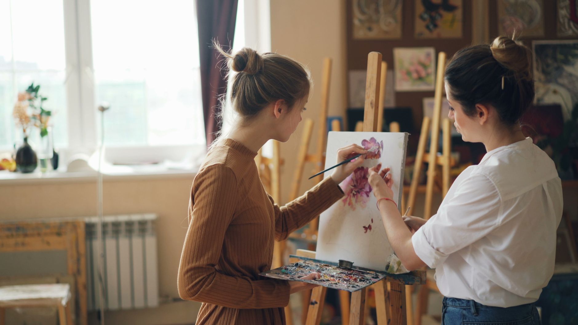 Client consultation and profiling — Young women painting flowers together in an art studio, capturing creativity.