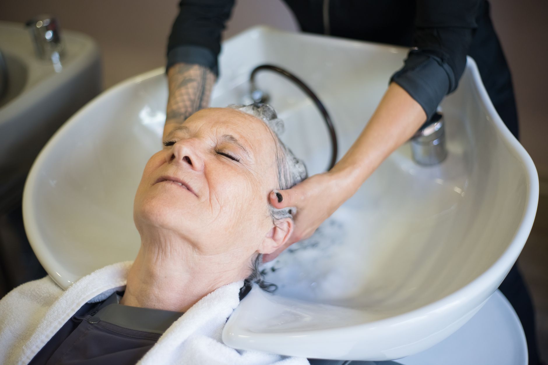 Dry spa and bathing experiences — Senior woman relaxing during a hair wash at a salon. the hairstylist gently massages her hair in an inviting, serene setting.
