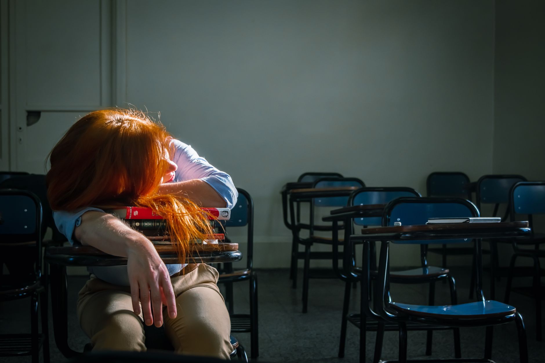 Holistic head, neck and shoulder massage — A tired student with red hair sleeps in an empty classroom under soft natural light.