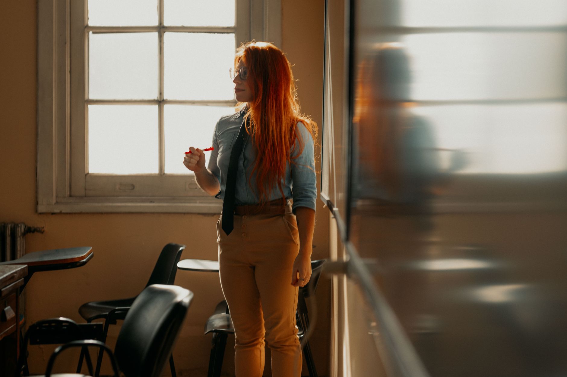 Thermal therapy massage — A university student with red hair stands by a window in a sunlit classroom.