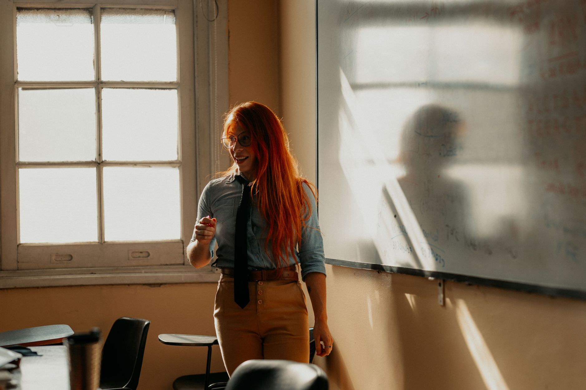 Implement health, safety, and hygiene — Smiling female teacher explains concepts on a whiteboard in a sunlit classroom in buenos aires.