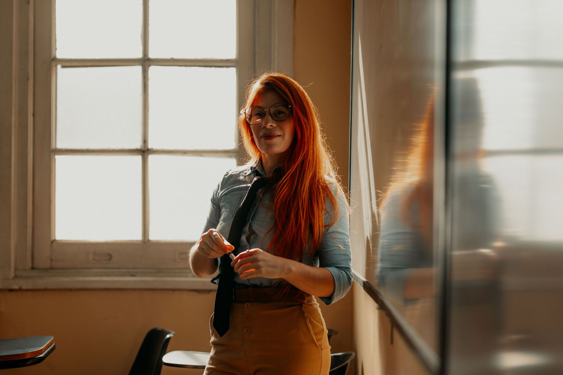 Client consultation and profiling — Smiling female teacher in buenos aires classroom during daylight, standing by the window with a chalkboard.