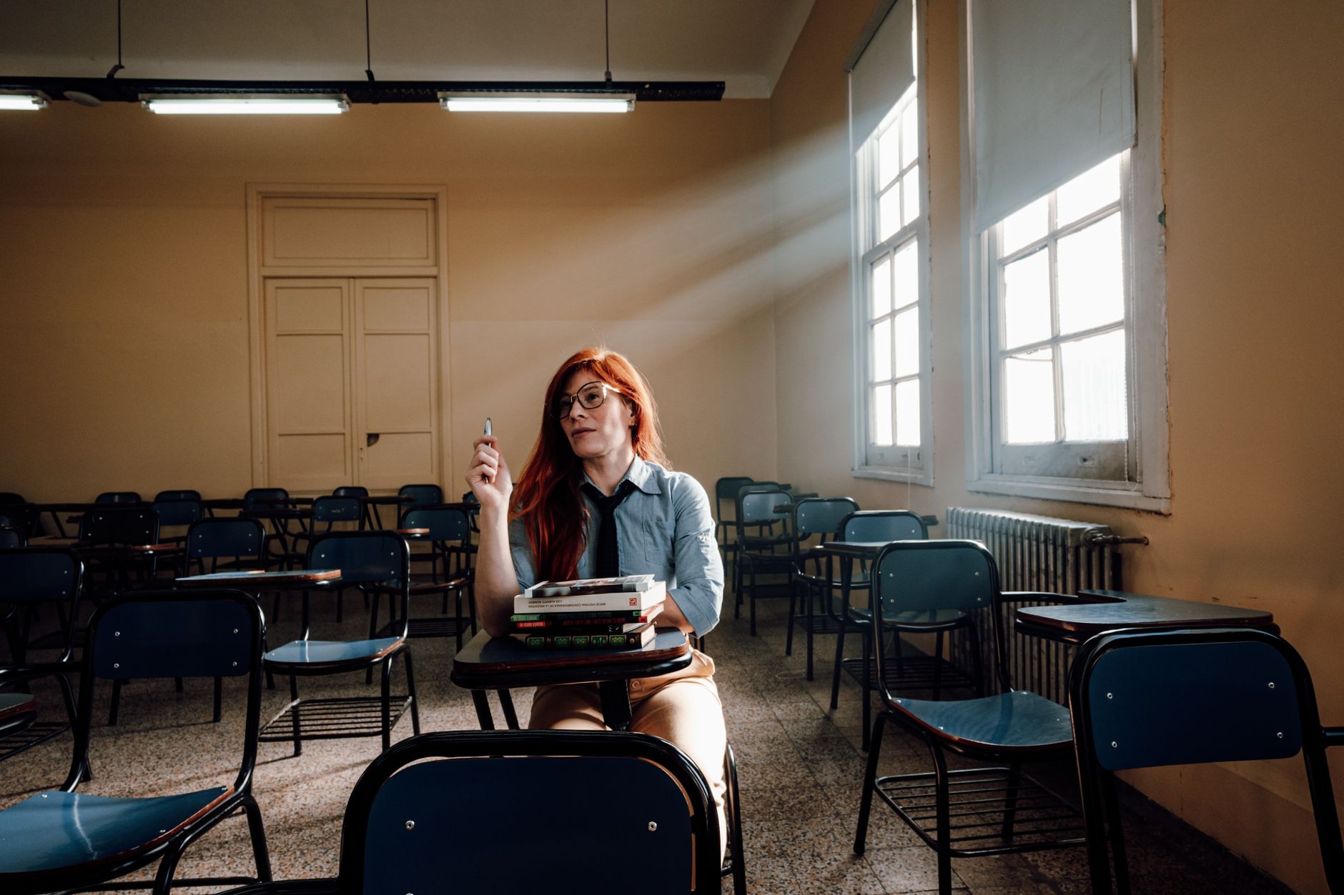 Body Massage — A lone student with red hair sits in an empty classroom in buenos aires, holding a pen.